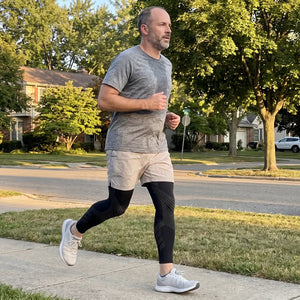 Man in his late 40s running in his neighborhood wearing TORVELL full-leg knee compression sleeves on both legs